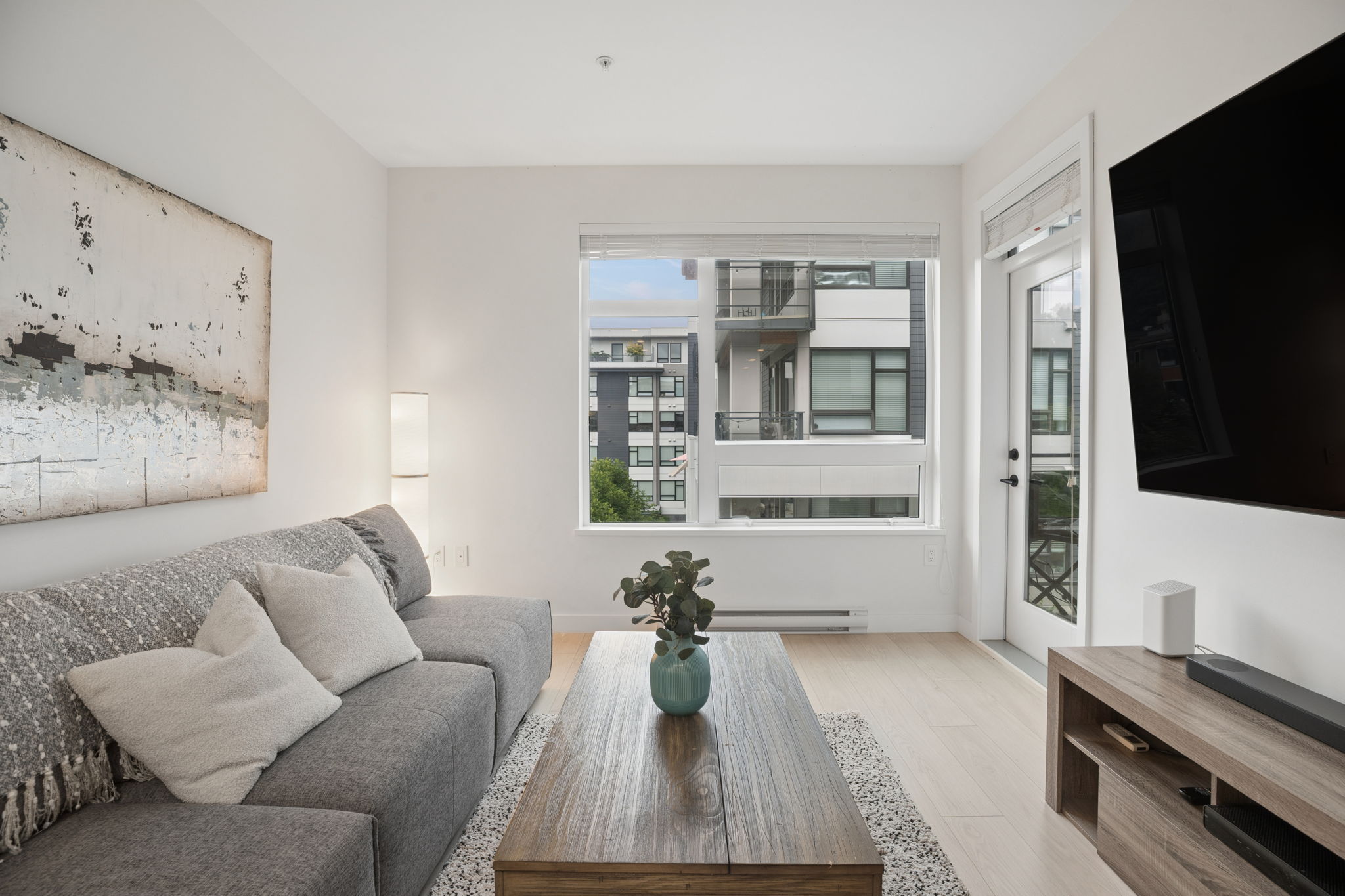 Living room with balcony access and wall-mounted TV at 413-3038 St George Street, Port Moody